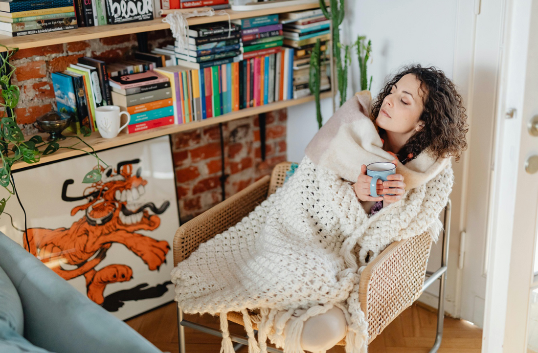 Lady wrapped in a warm blanket with a warm drink when she feels cold